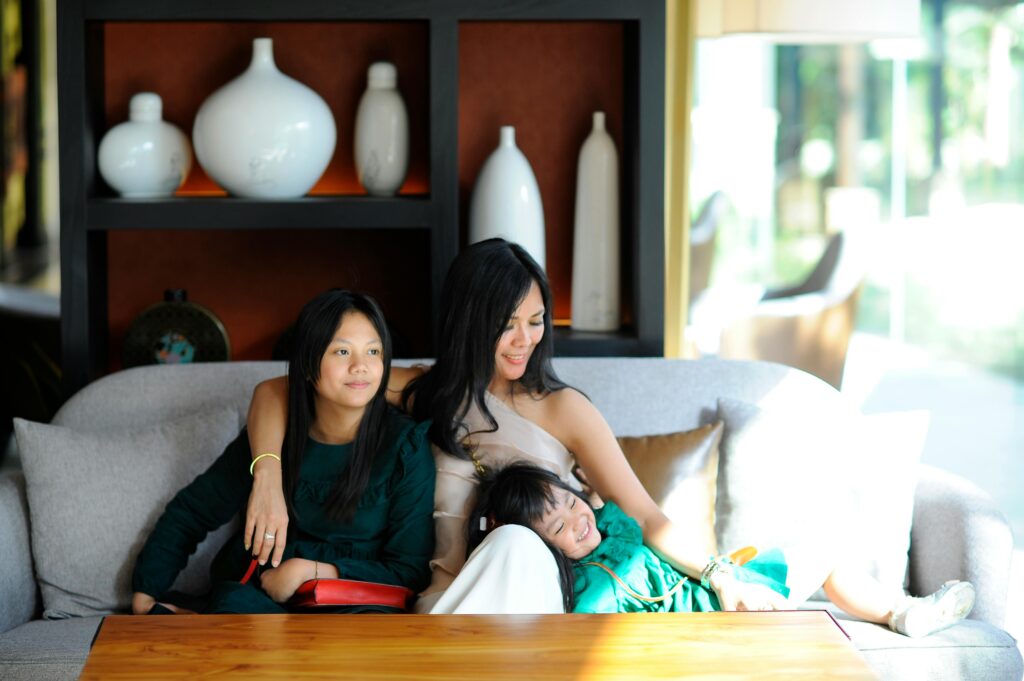 A mother and her daughters enjoy a sunny day indoors on a comfortable couch.