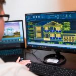An architect reviews detailed house designs on dual monitors in a modern office setting.