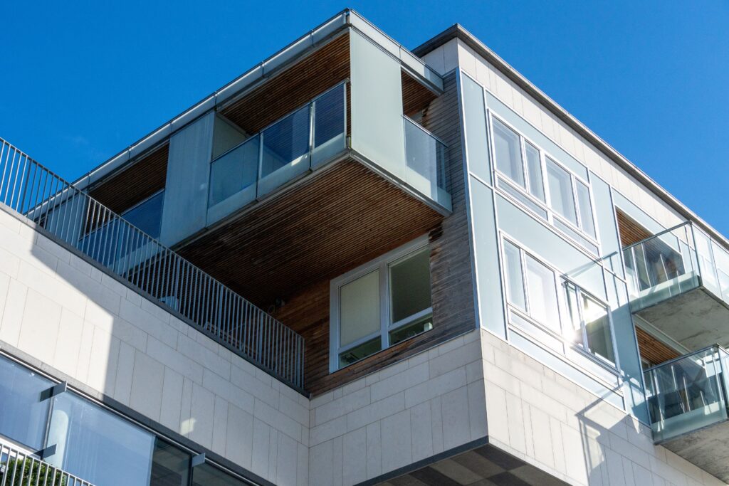 Low angle view of a modern residential building with glass balconies under a clear blue sky.