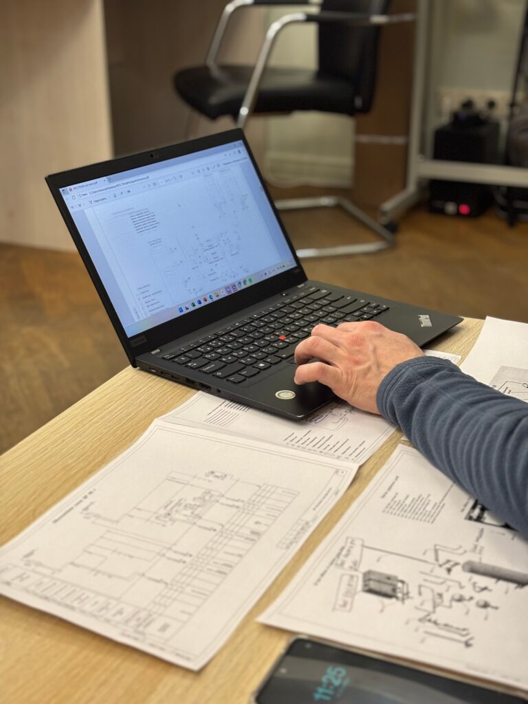 PH5 CPHD/C Exam An engineer works on a laptop reviewing technical blueprints and diagrams in an office.